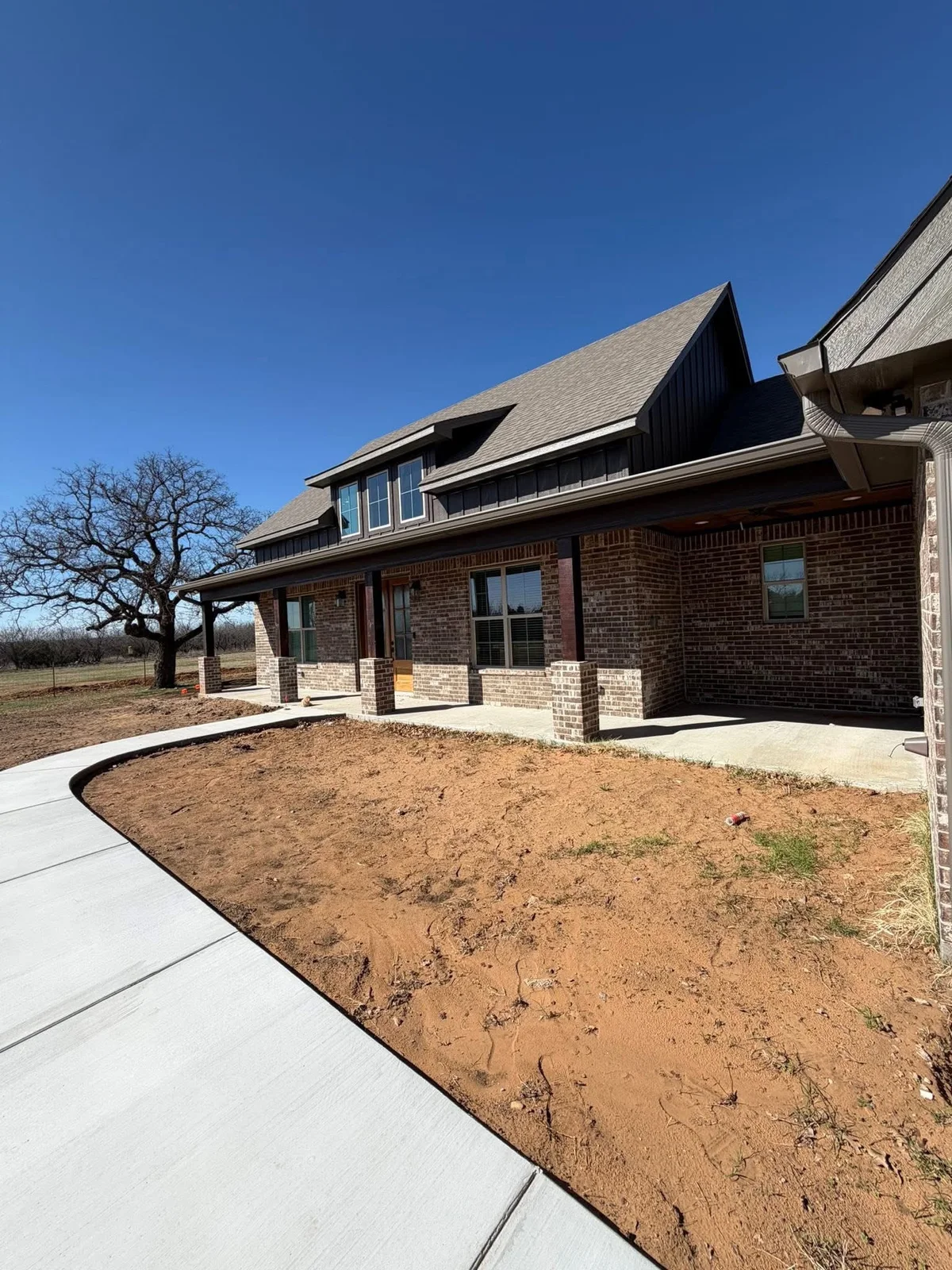 Brick house exterior with dark upper siding and a curved concrete driveway
