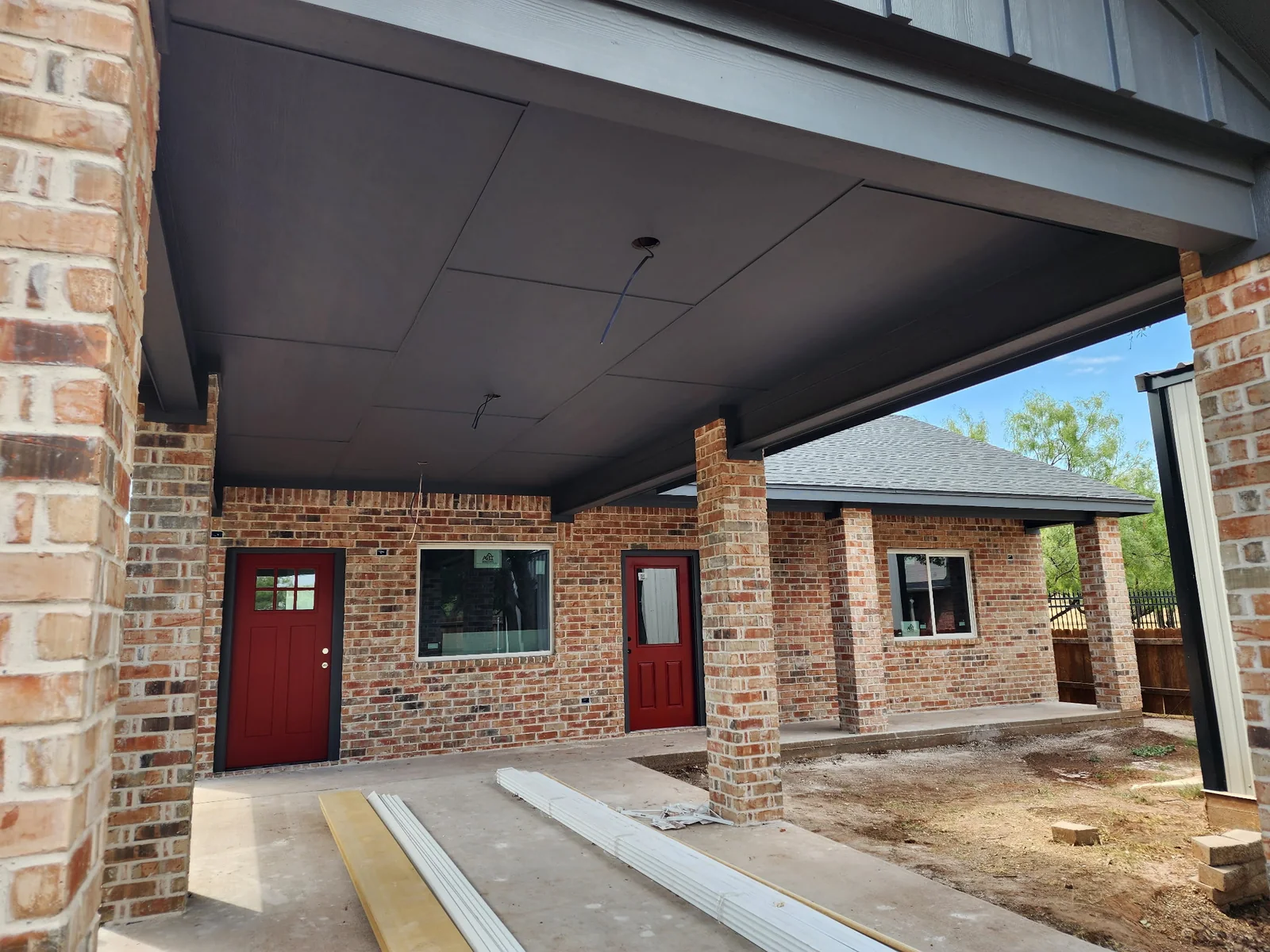 Dark gray covered-entry ceiling above brick columns and red doors