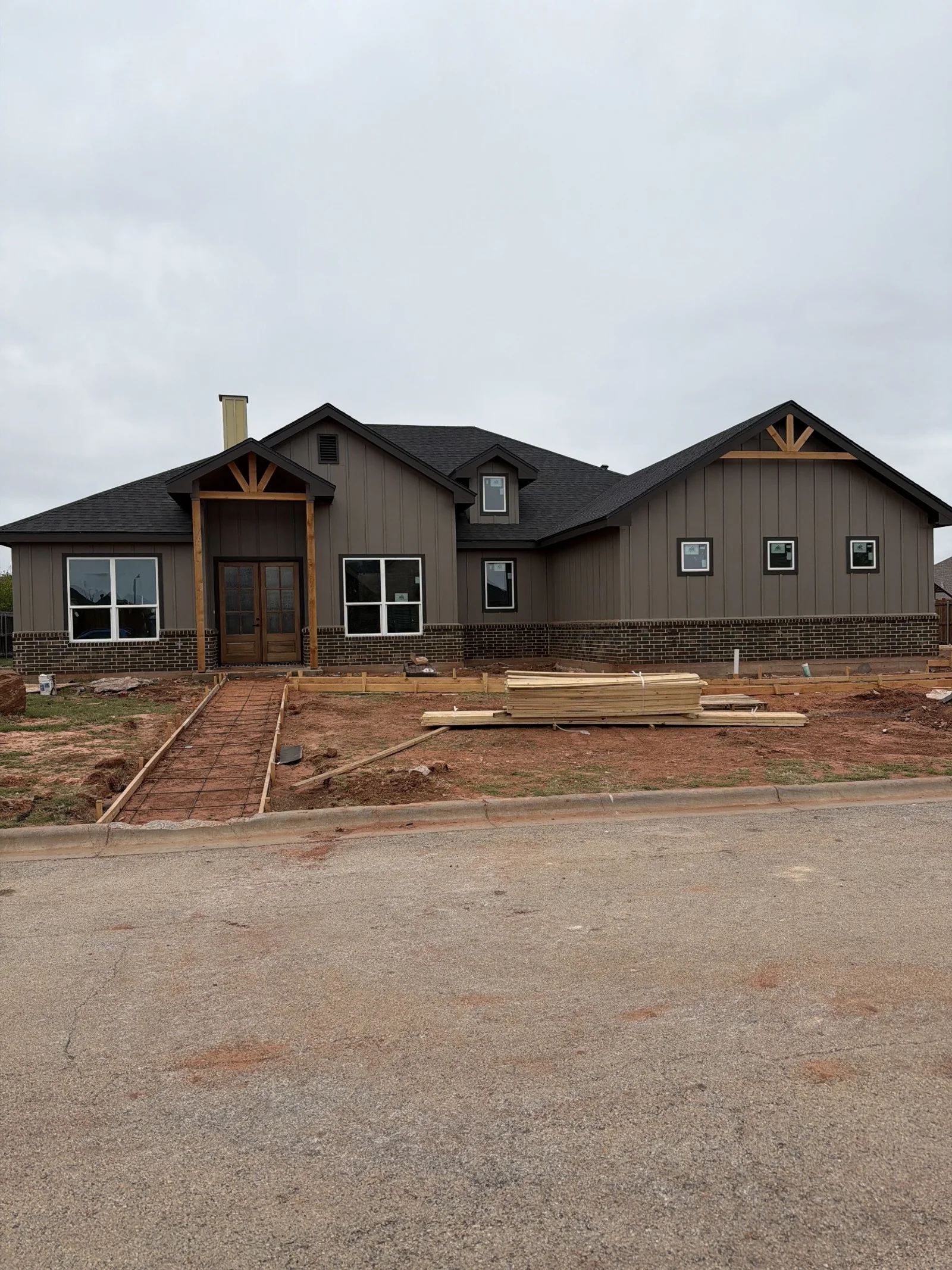 Gray-brown siding, brickwork, and timber accents on a house front with unfinished walkway forms