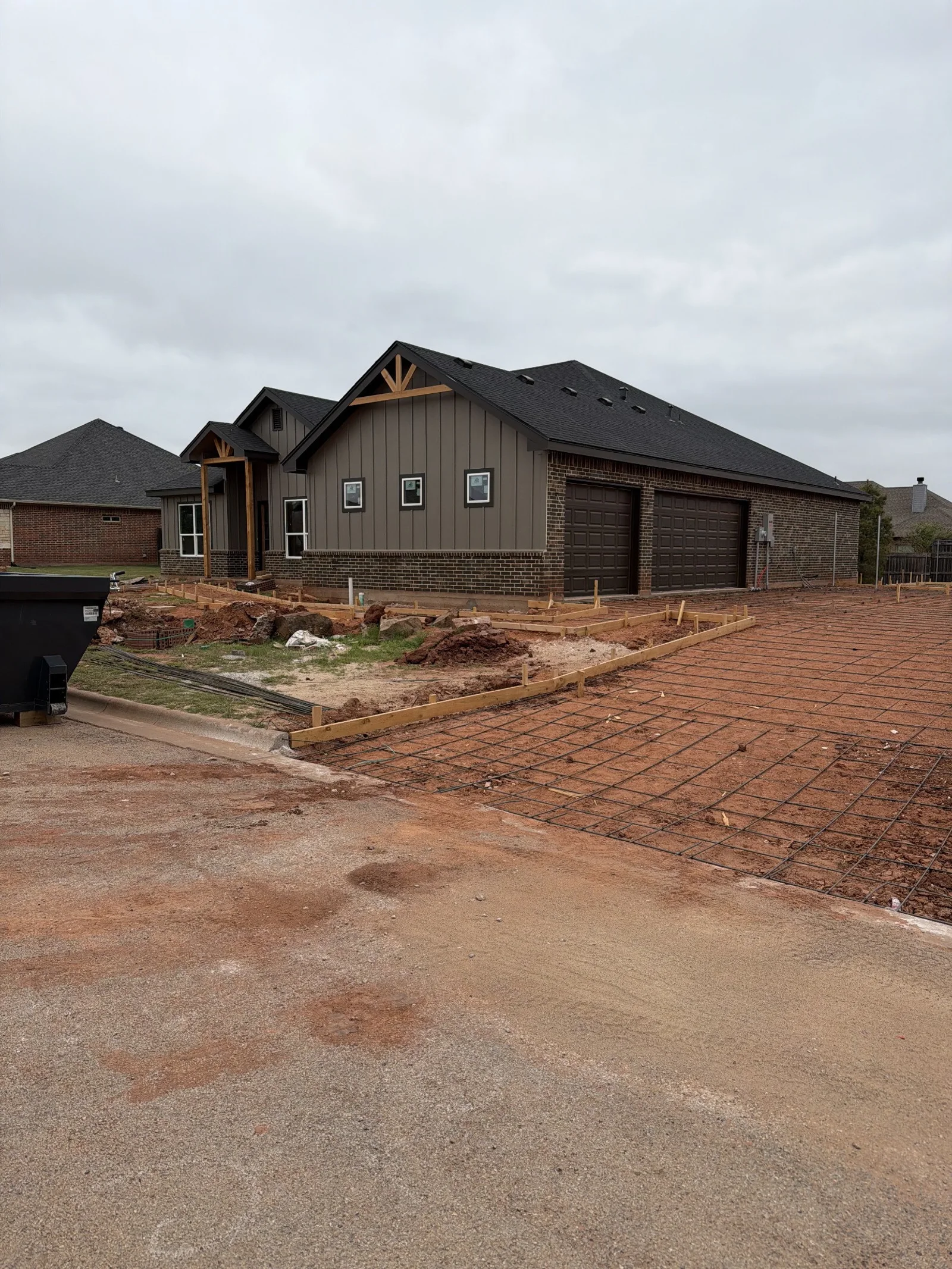 Gray-brown siding, brickwork, and two garage doors beside driveway forms
