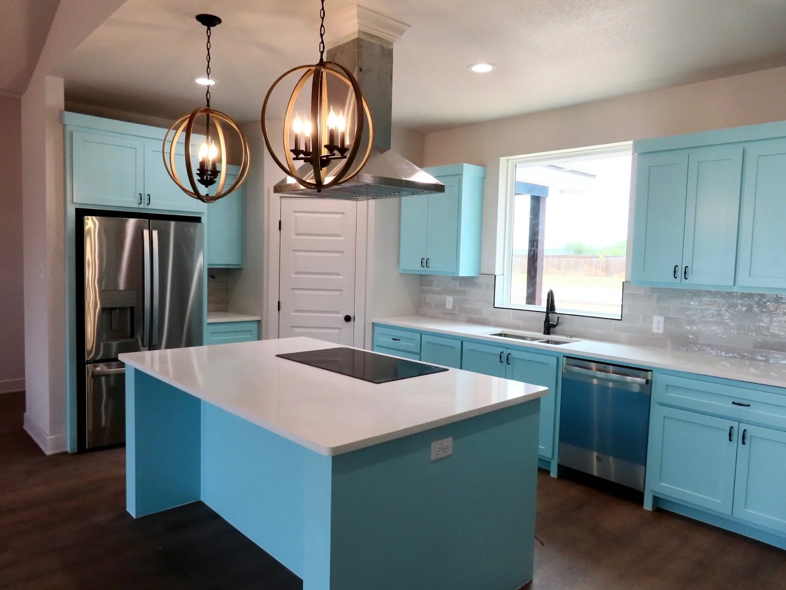 Turquoise kitchen island and cabinets beneath pendant lights