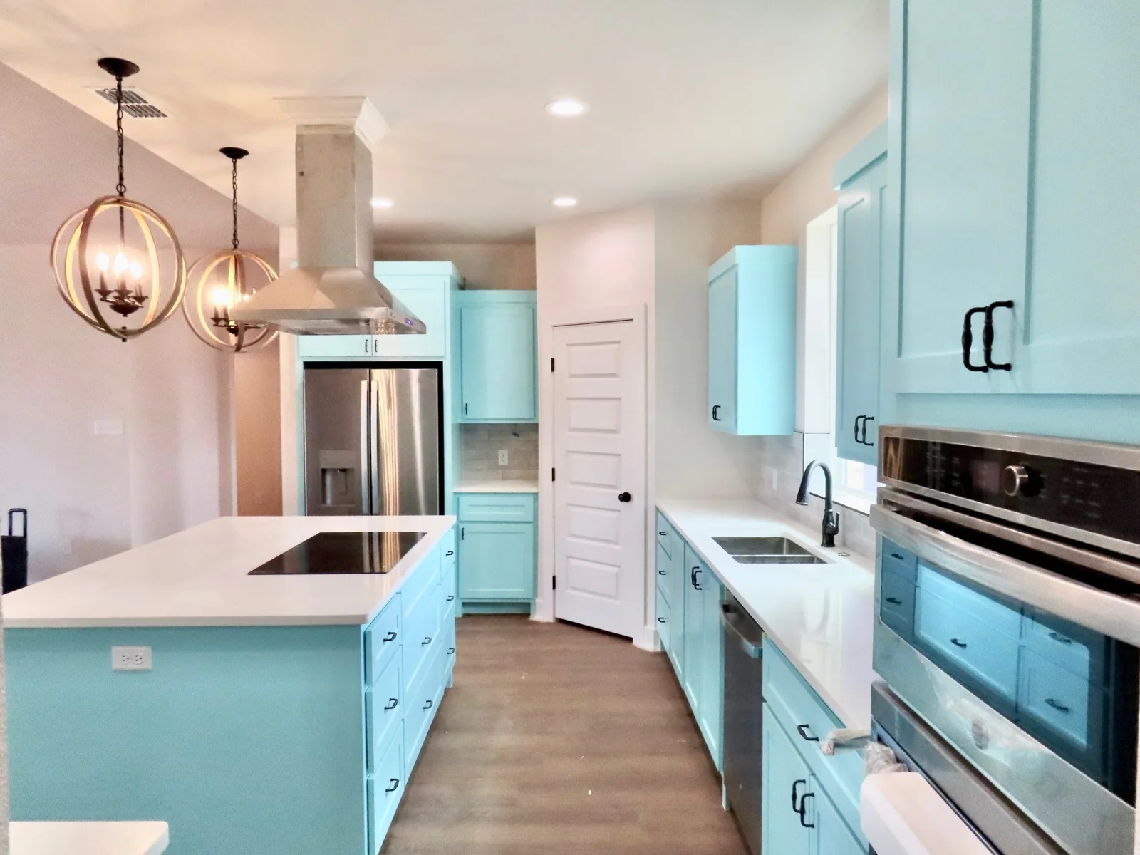 Turquoise kitchen cabinets beside a built-in oven and white counters