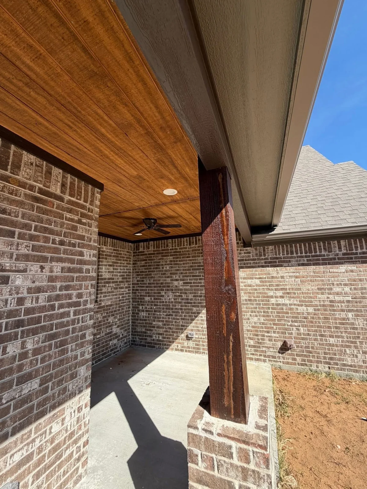 Wood porch ceiling with recessed lights and a fan above brickwork